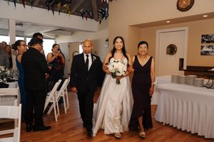 Wedding guests gather in a warmly lit indoor reception venue with elegant white table settings and decor.
