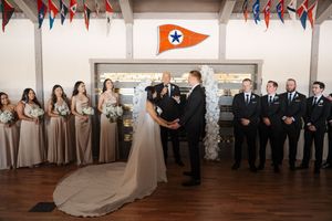 A wedding ceremony moment showing a line of groomsmen standing against a wall with flags and decor.