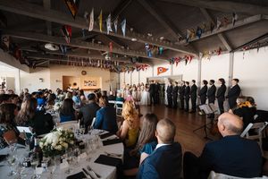 Reception guests gather in a modern banquet hall decorated with hanging string lights and flags for a celebration.