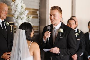 Wedding party members share joyful laughter while gathered near a white floral arch during the ceremony.