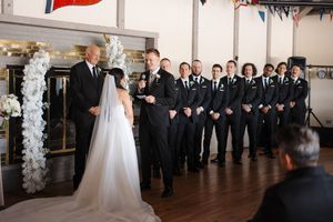 Wedding party in formal attire lined up in an elegant venue with decorative balloon columns.