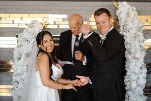 Wedding celebration with guests gathered near an elegant white floral arch during an indoor ceremony.
