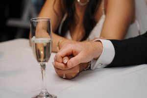 Close-up of clasped hands at a formal event with a champagne glass on white tablecloth.