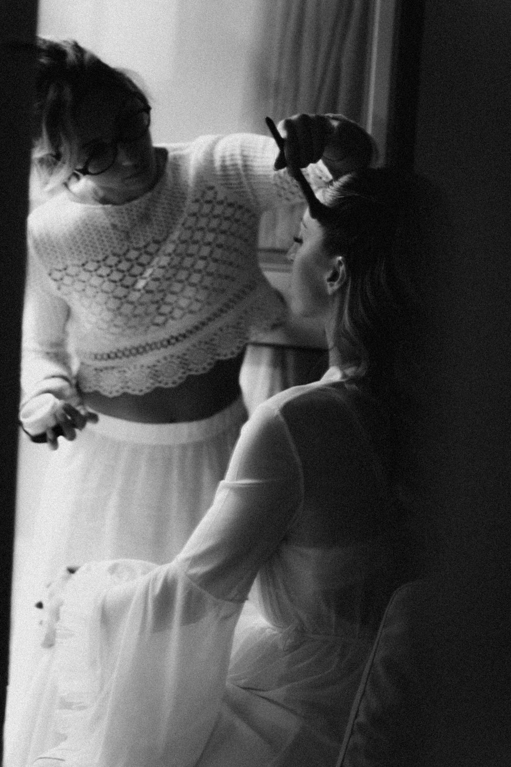 Black and white photo series showing bride getting ready by window in lace gown with dramatic lighting.