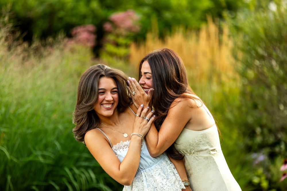Two friends share a joyful laughing moment together in a garden with tall grass and flowers in the background.