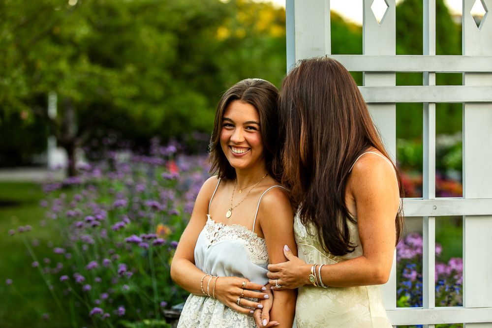 Two people embrace and laugh together in a lush garden setting with a white trellis and purple flowers.