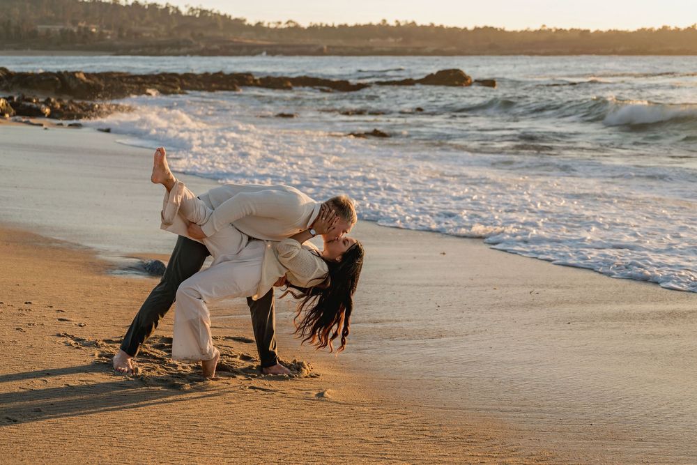 People walk along a sandy beach at sunset with gentle waves rolling onto the shore.