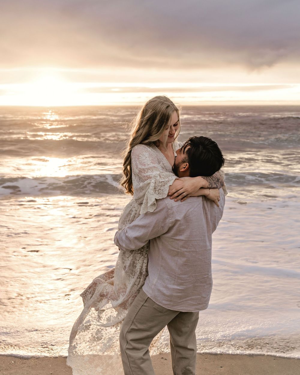 Two people share a romantic embrace on the beach at sunset, their silhouettes framed by the golden light and crashing waves.