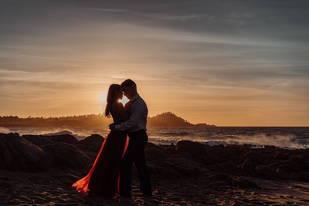 Silhouette of couple against dramatic sunset sky with ocean waves crashing in the background.