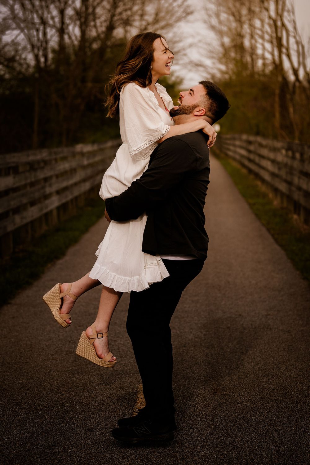 Couple embracing and spinning on a wooded path at sunset creating a romantic outdoor moment.