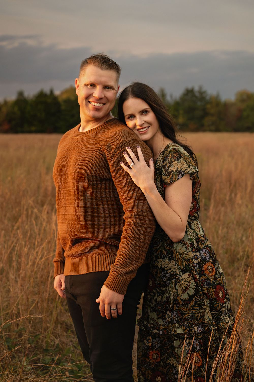 A couple embraces and smiles together in a golden autumn field at sunset.