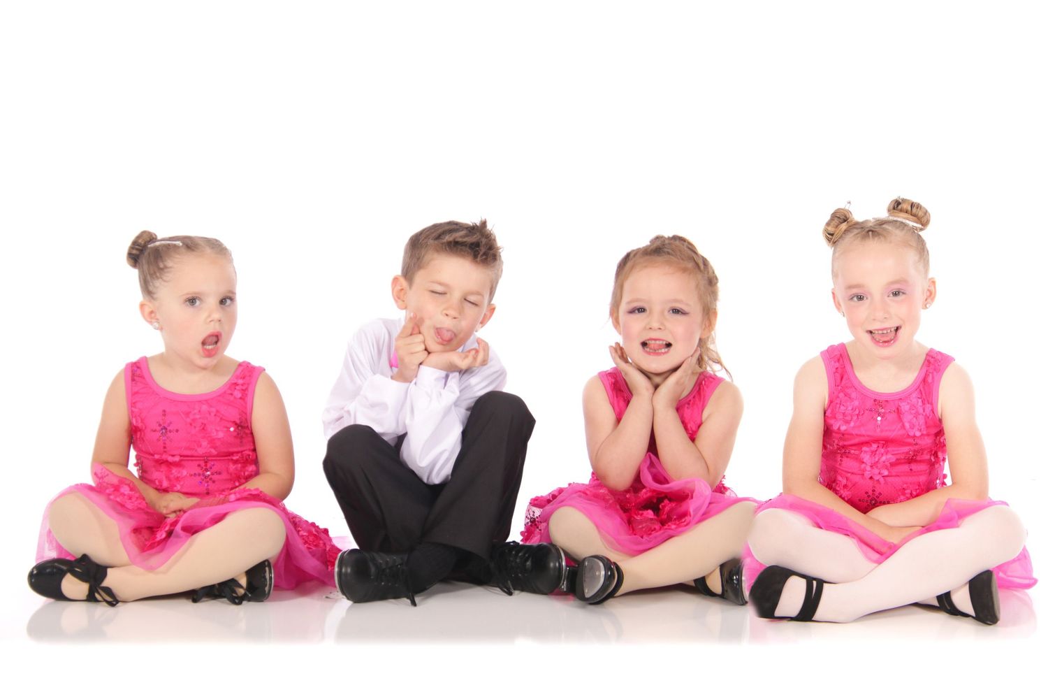 Young dancers in pink tutus lie in row during dance recital photoshoot.