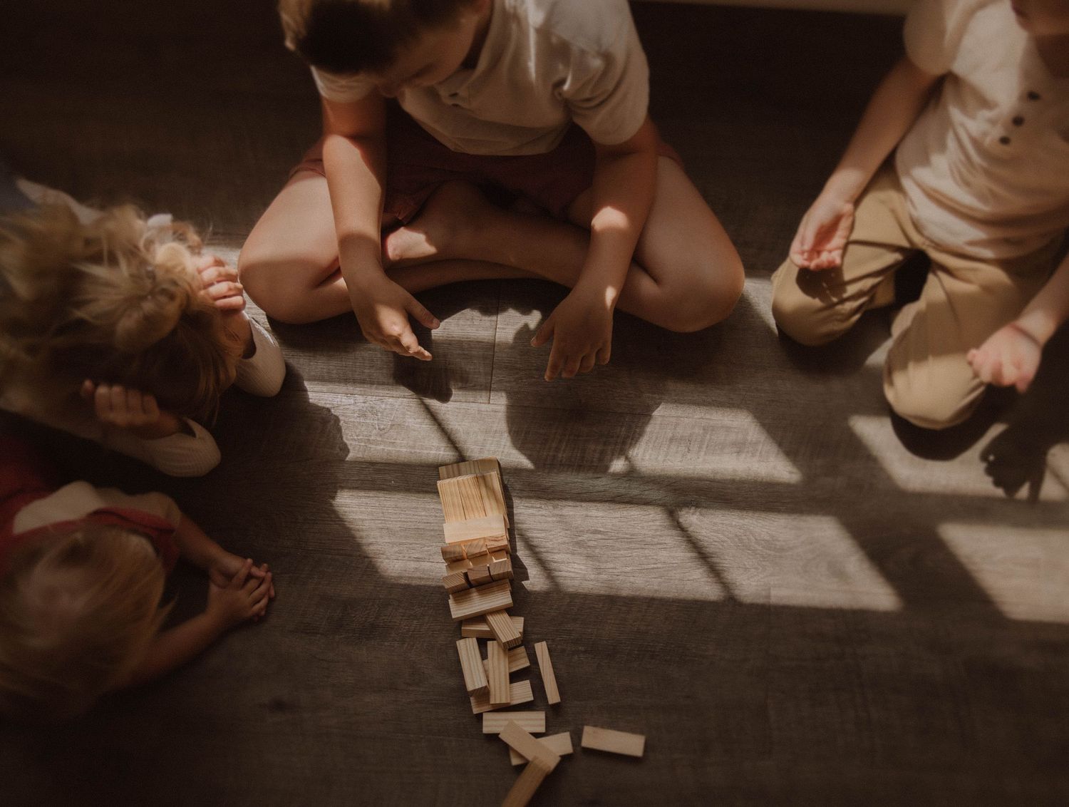 Wooden building blocks arranged in various patterns on a dark floor during indoor playtime activities.