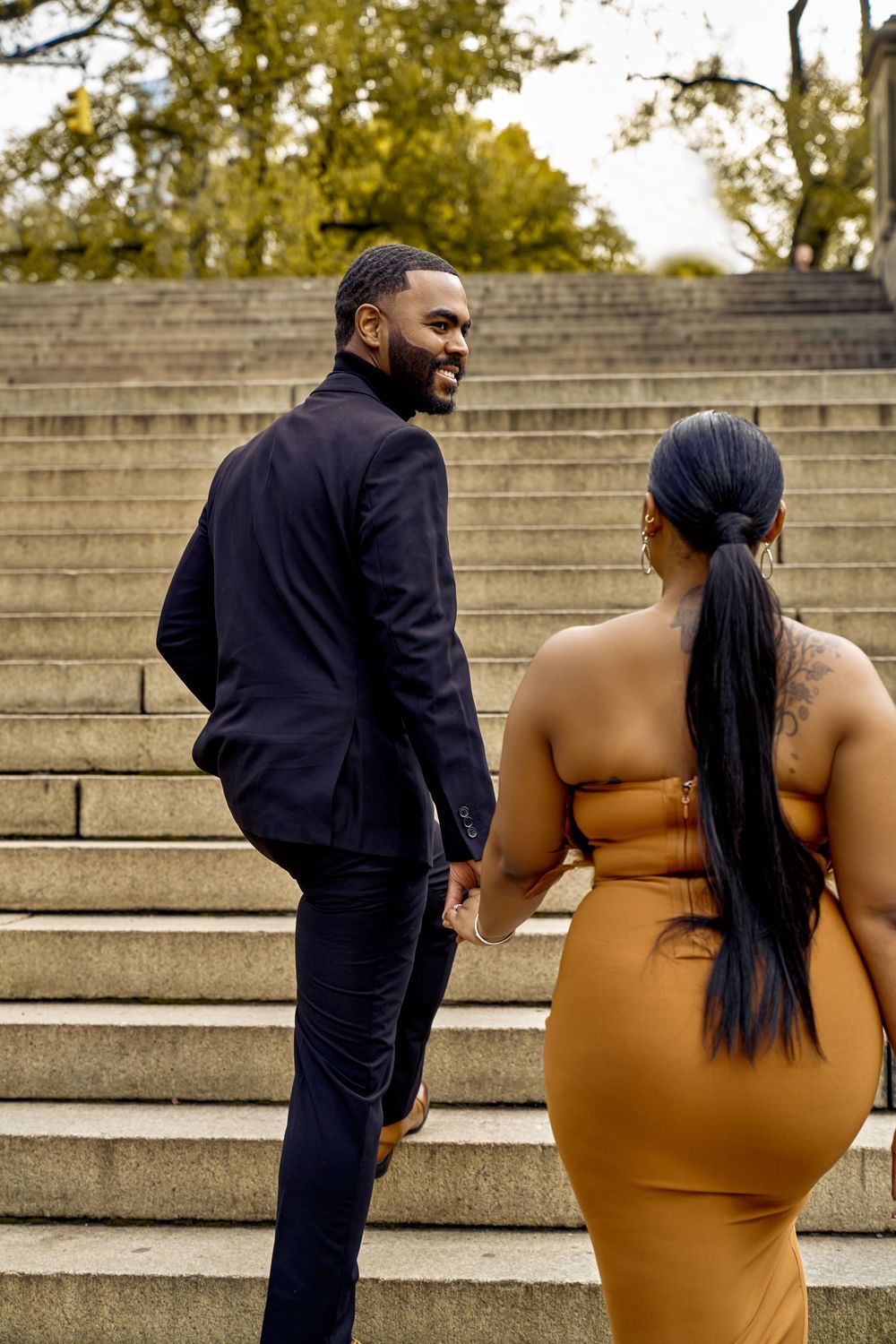 Couple dressed elegantly in navy suit and brown dress stand together on outdoor stone steps.