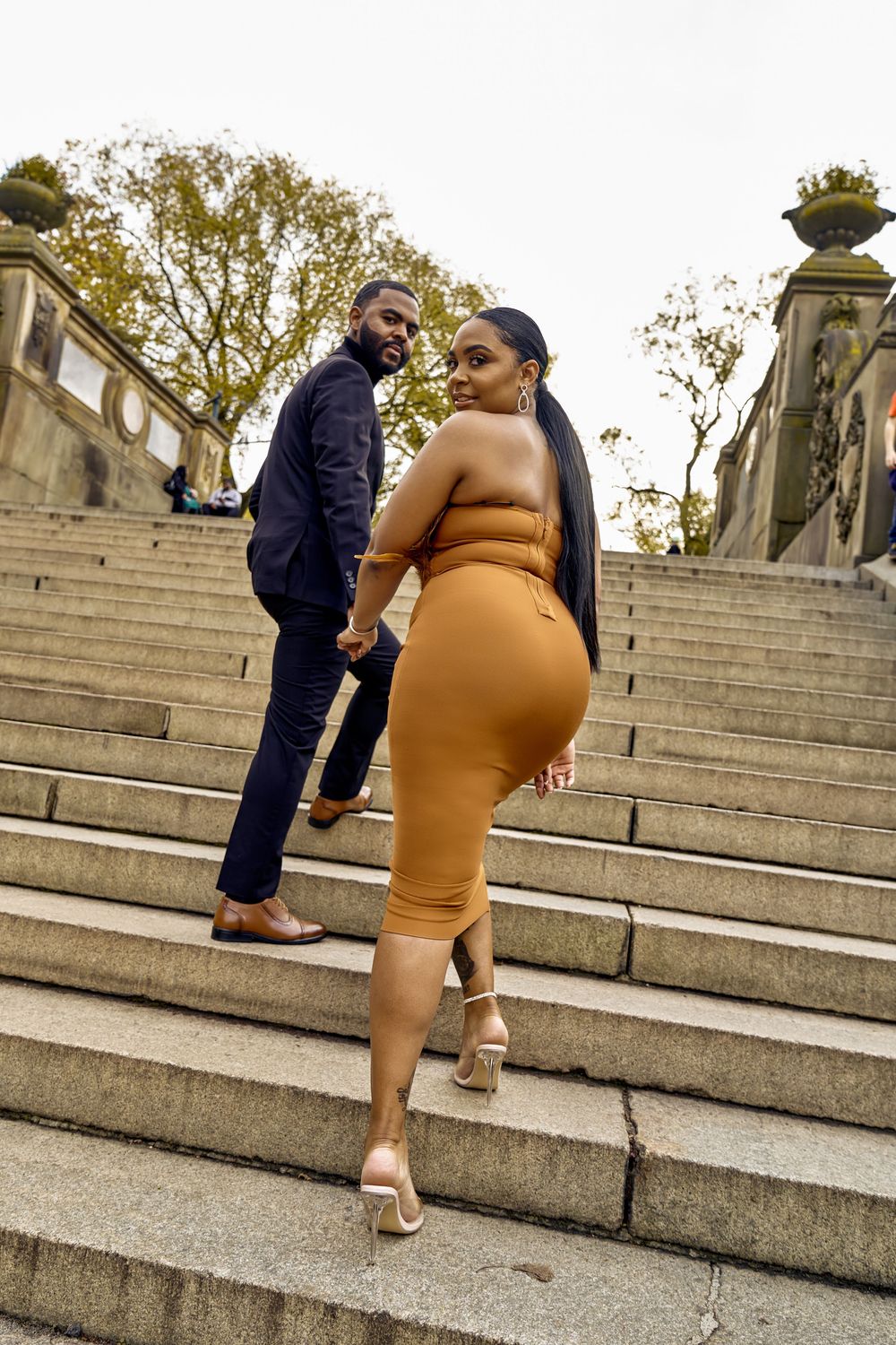 Couple in formal attire walking up outdoor stone steps during golden hour.