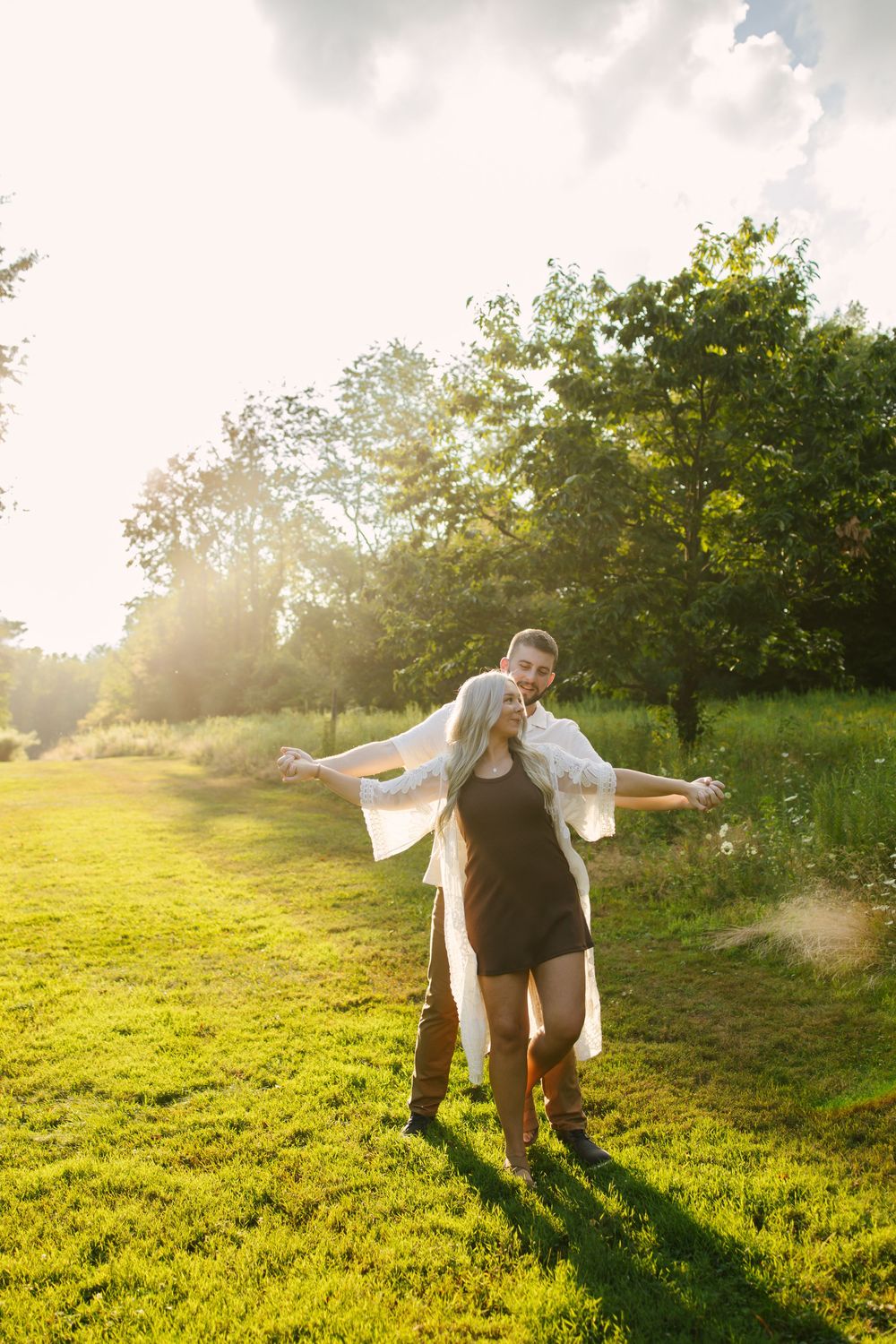 Couple dances and spins in a sunlit meadow during golden hour.