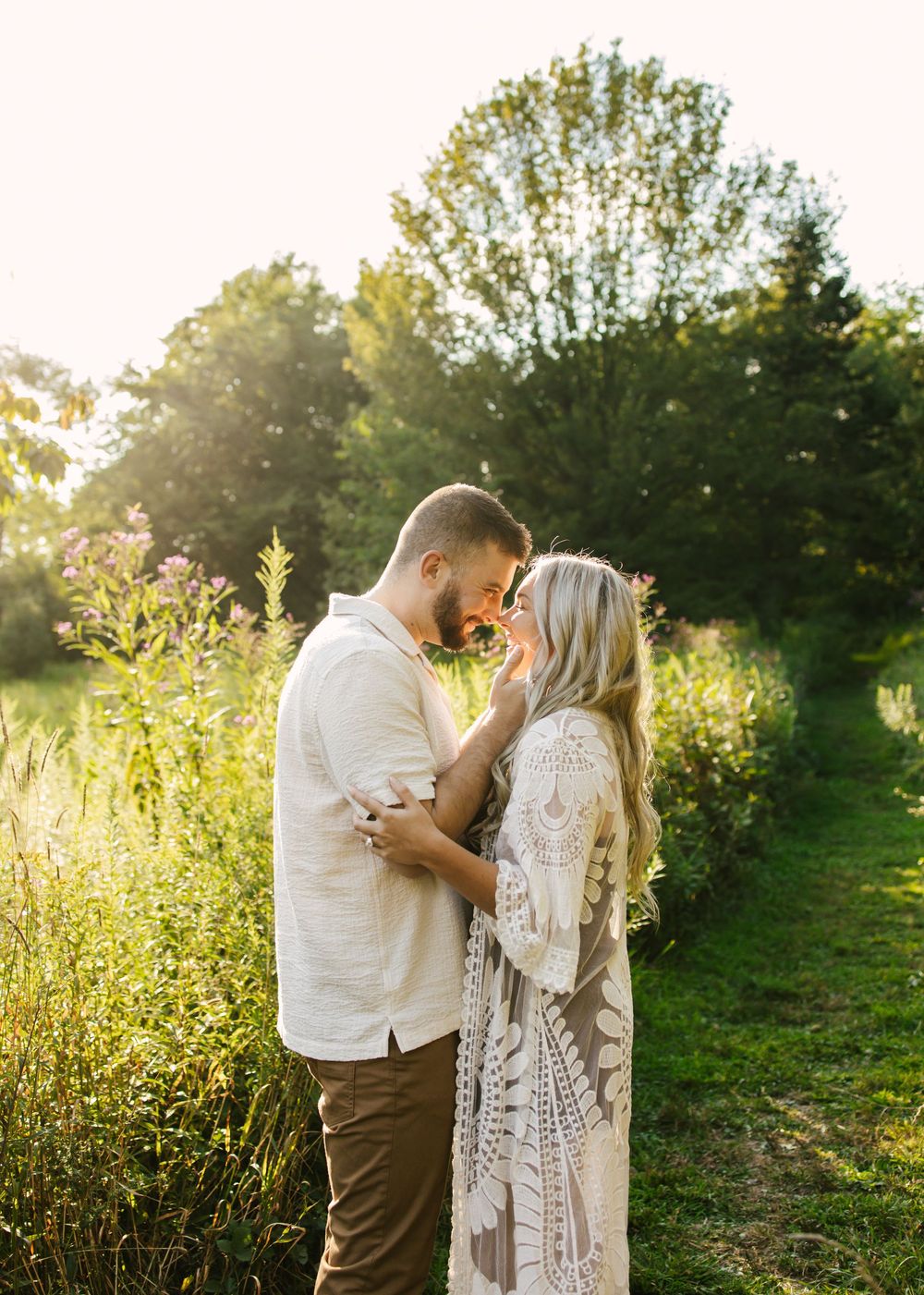 Couple embraces in golden sunlight among wildflowers during romantic outdoor photoshoot.