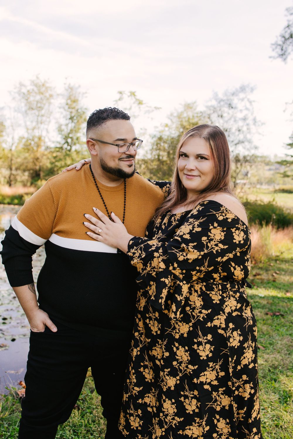 A couple wearing coordinated black and gold outfits embrace while posing outdoors in a natural setting.