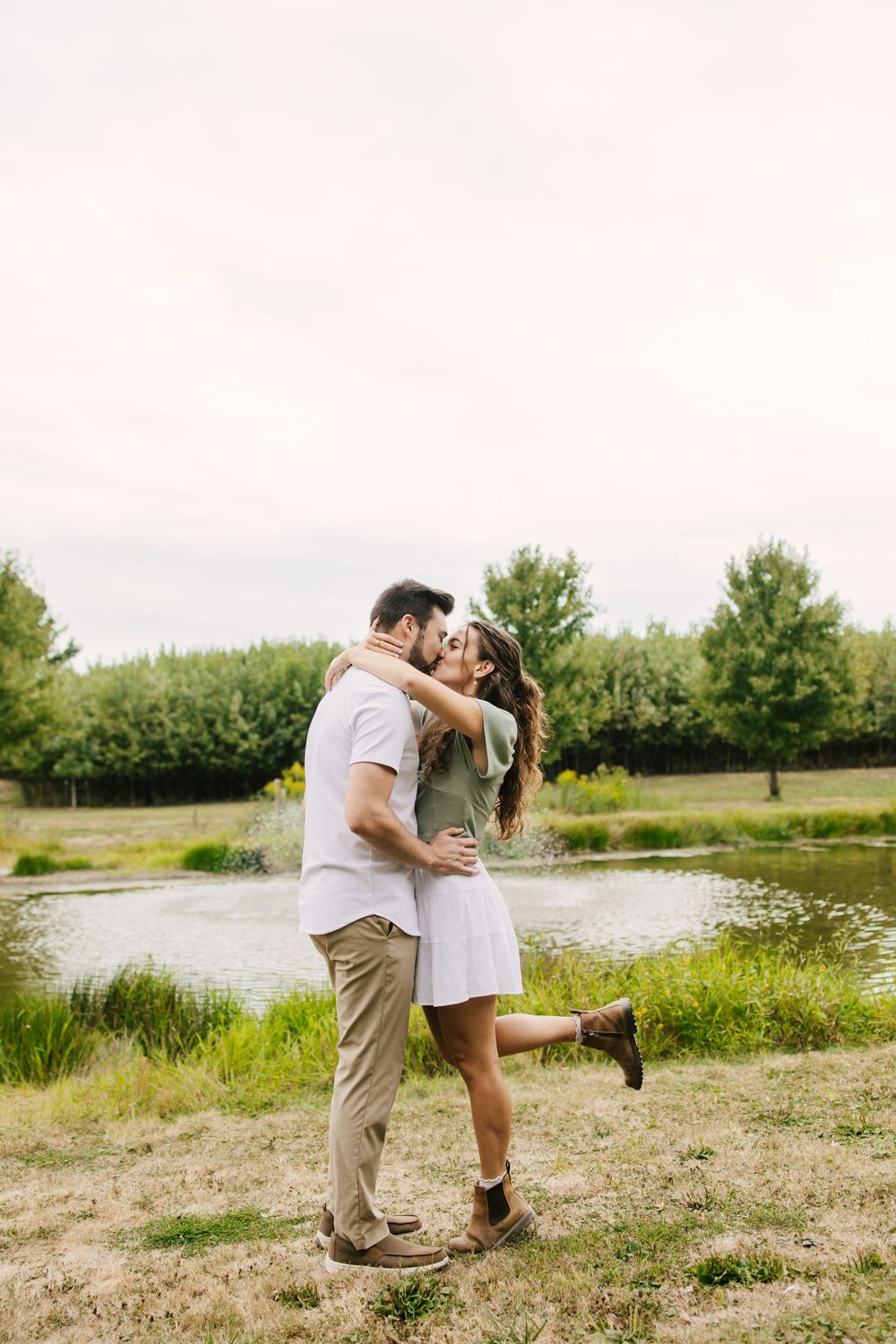 Couple sharing tender moments by a serene lakeside with green foliage.