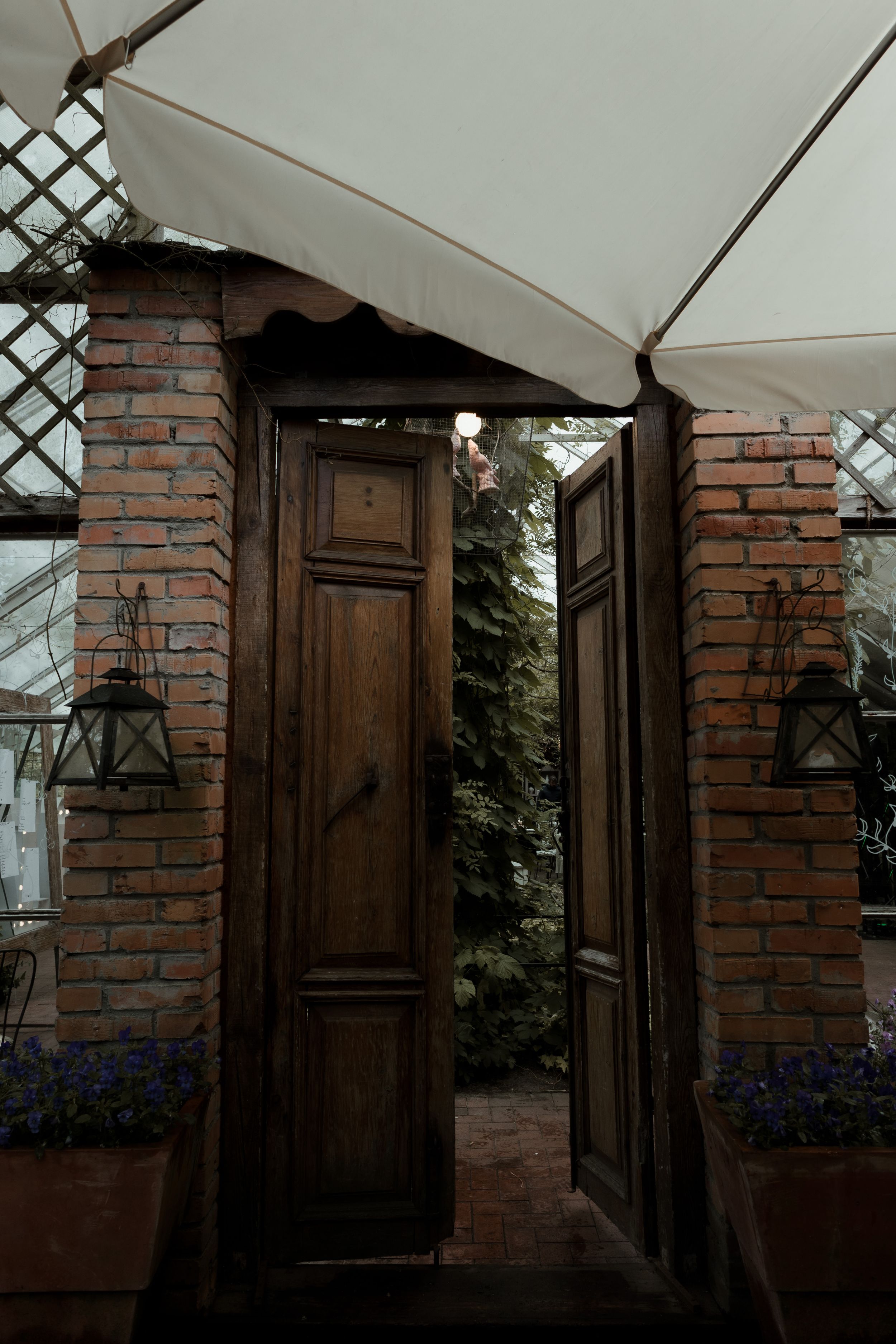 Rustic wooden double doors with brick columns and white awning create an elegant garden entrance.