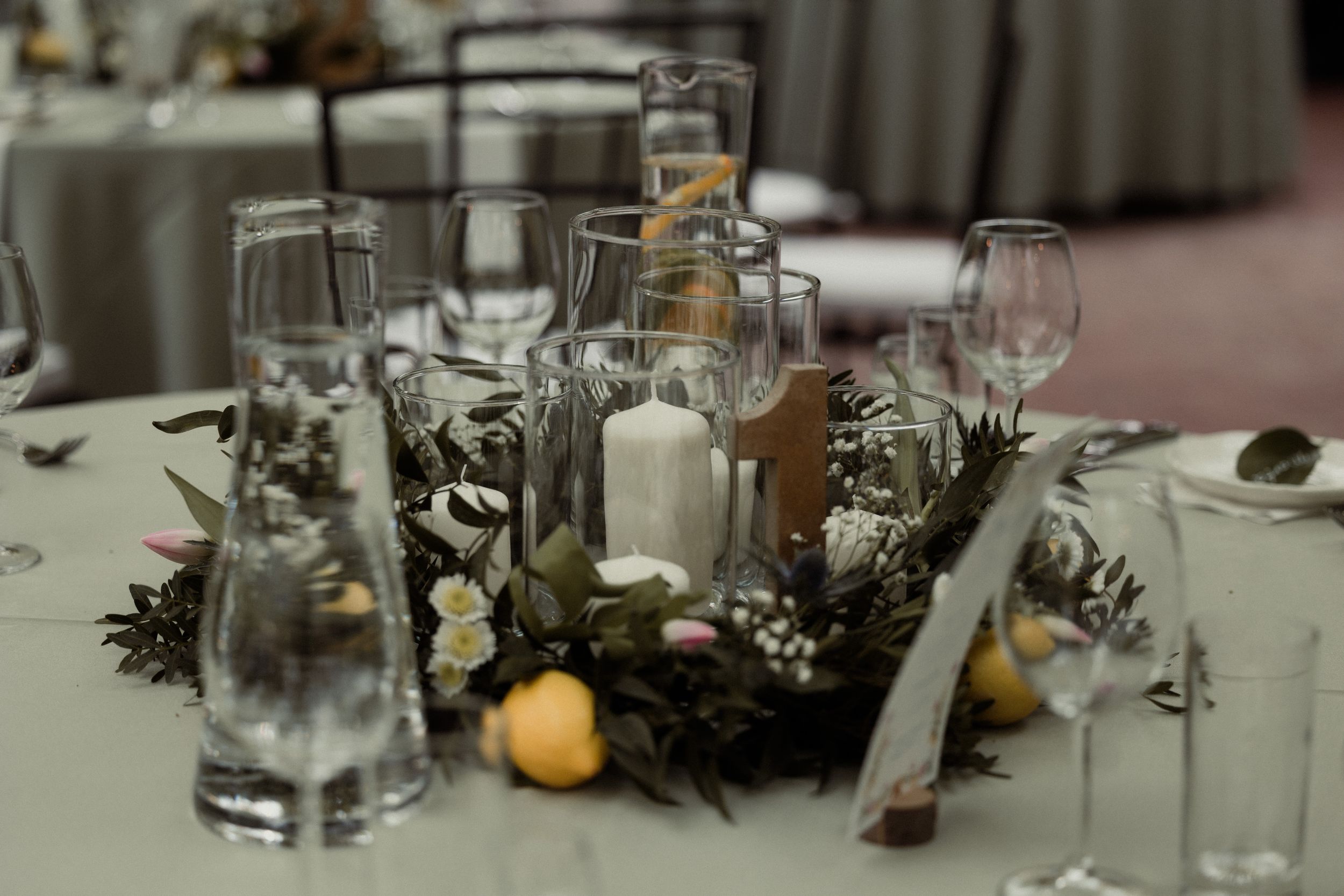 Beautiful table setting with glass candleholders, greenery garlands and small pumpkin accents at an elegant event.
