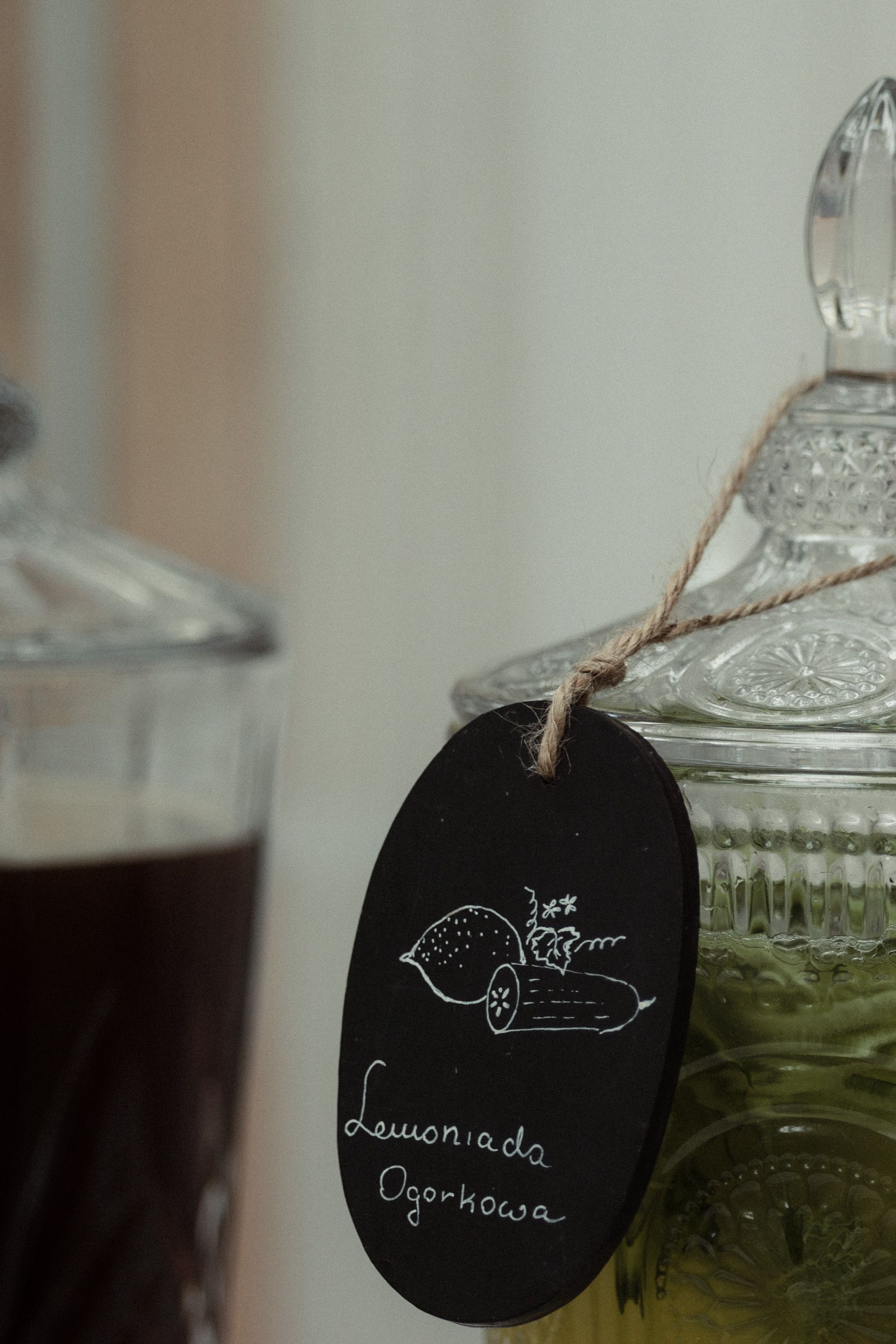 Glass jar with a black chalkboard tag showing lemonade cucumber drawing and text against a light background.