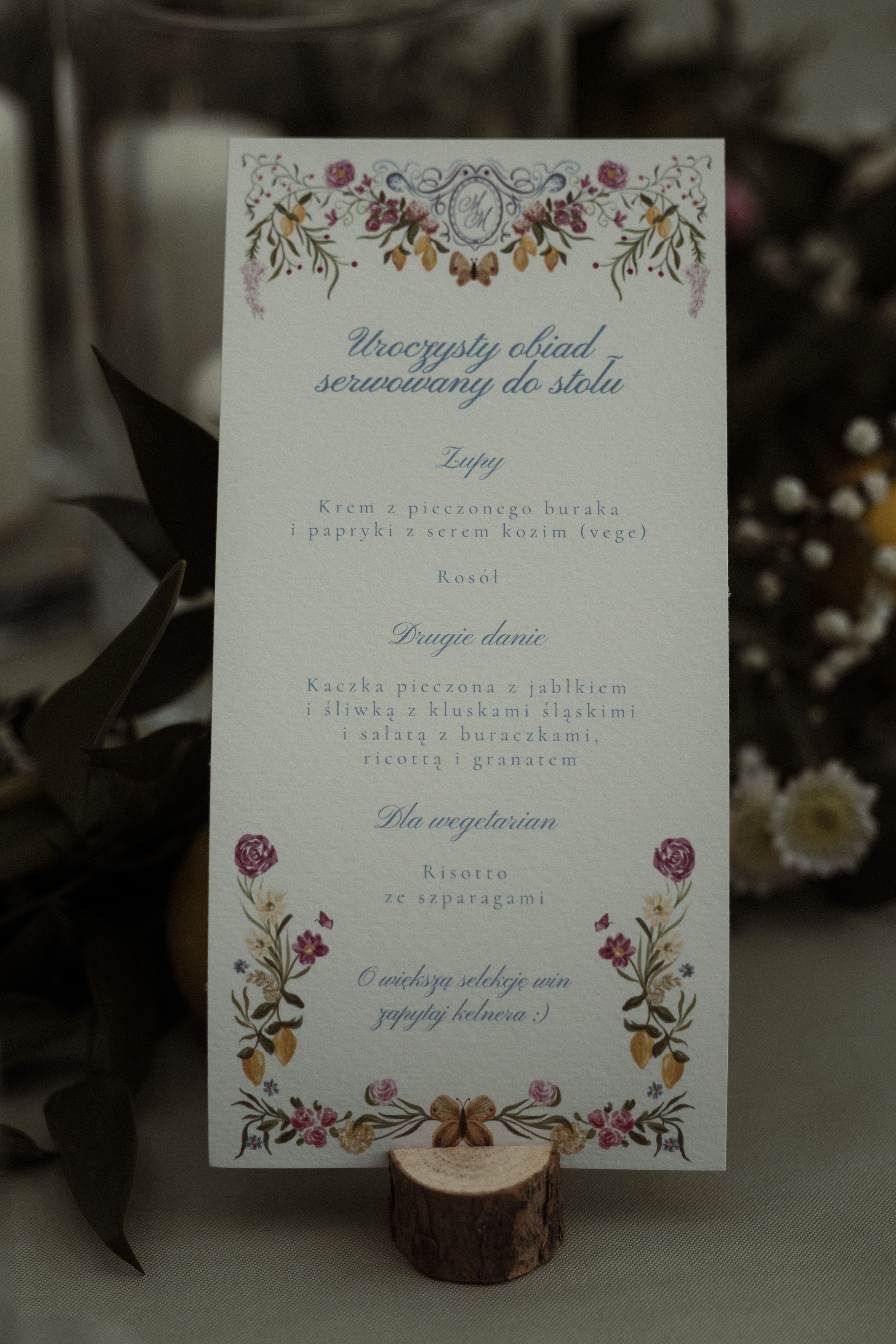 A decorative wedding menu card with floral designs rests on a small wooden stand against a dark background.