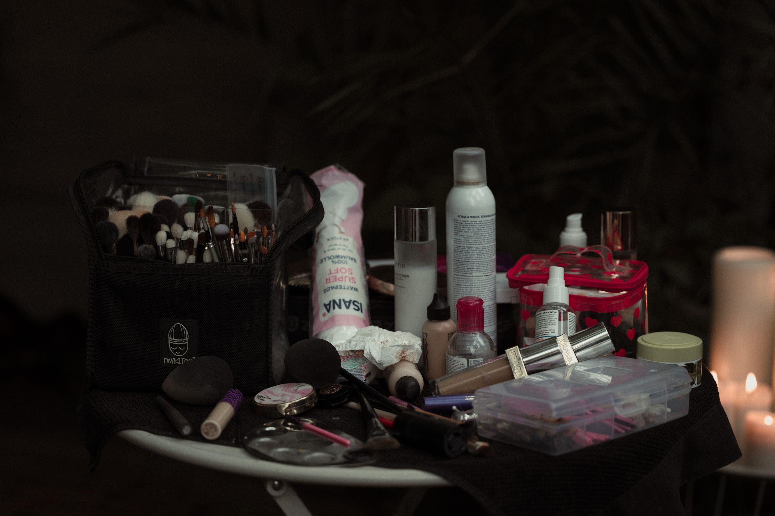 Various personal items and products are arranged on dark surfaces in low lighting conditions.