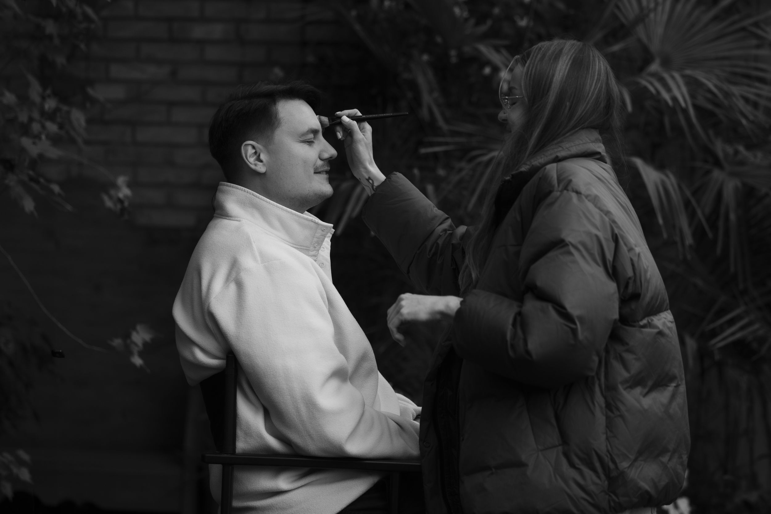 Black and white photo of someone getting their makeup done by a makeup artist outdoors.