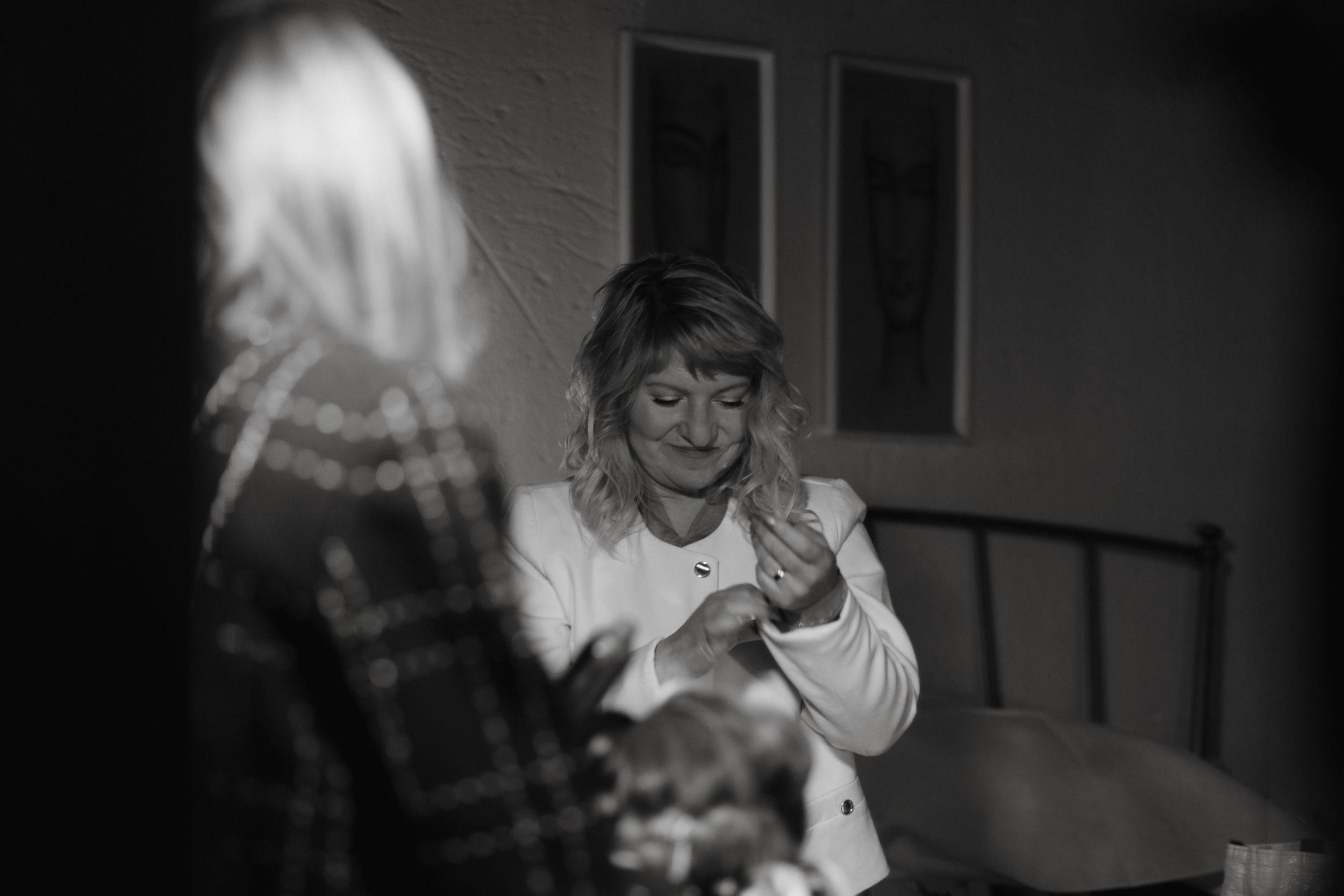 A person in a white top examines something held in their hands at a dimly lit table in black and white photograph.