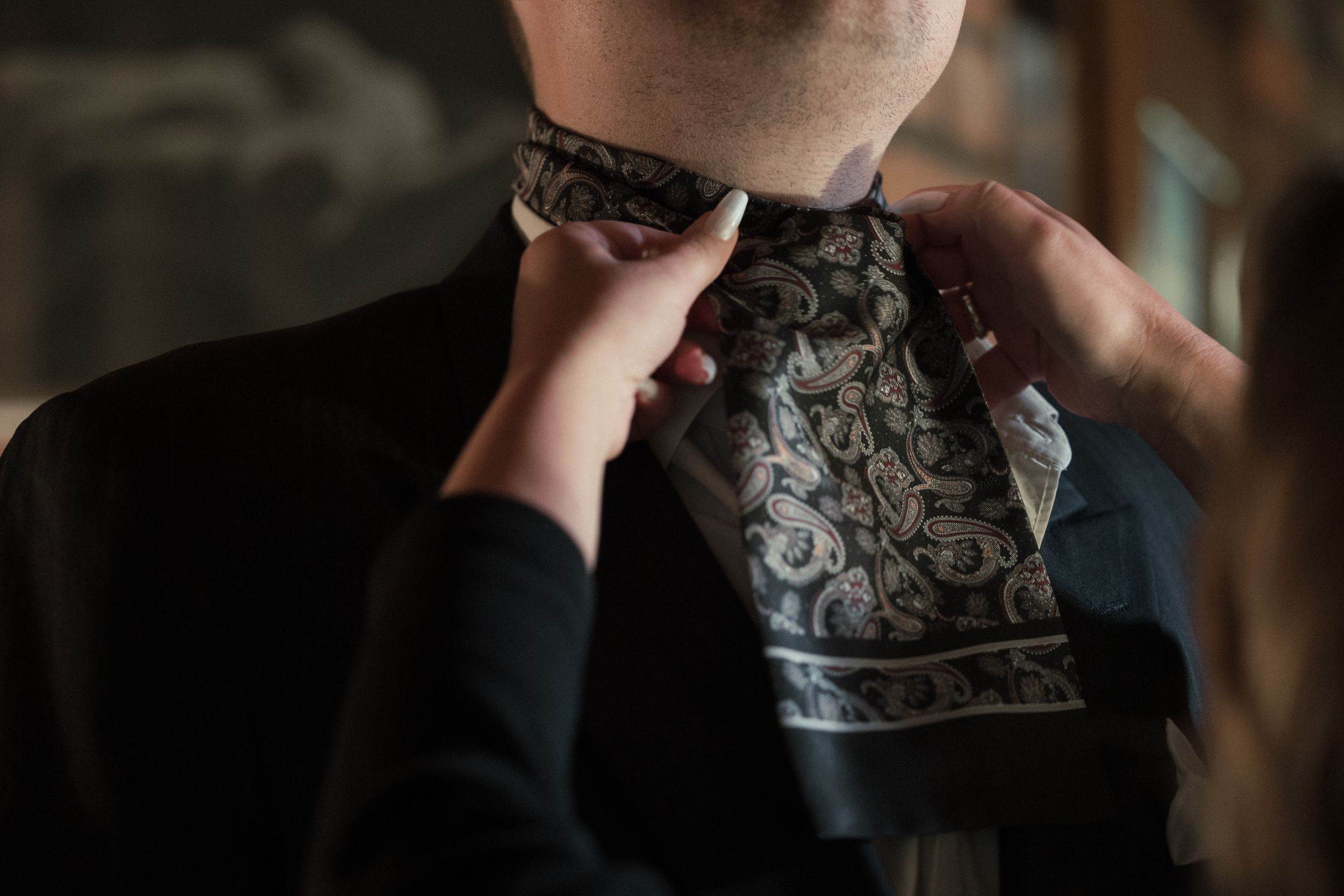 Person putting on a patterned silk bandana around their neck in dim lighting.