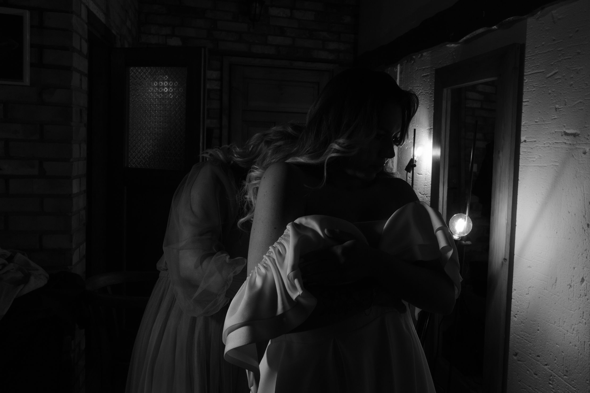 A group of people stand in a dark hallway illuminated by a single light source in black and white.