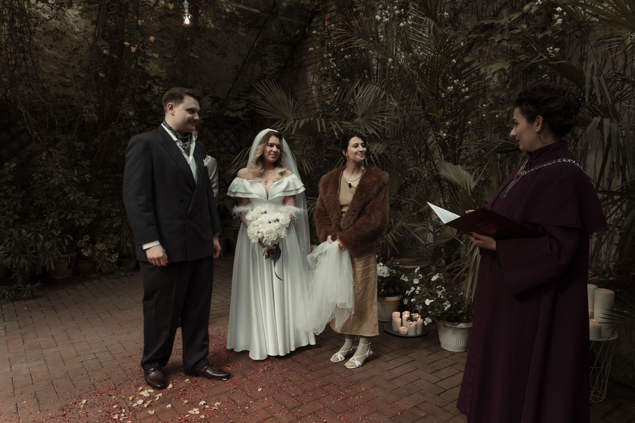 Outdoor wedding ceremony on brick path with small group gathered in rustic garden setting.