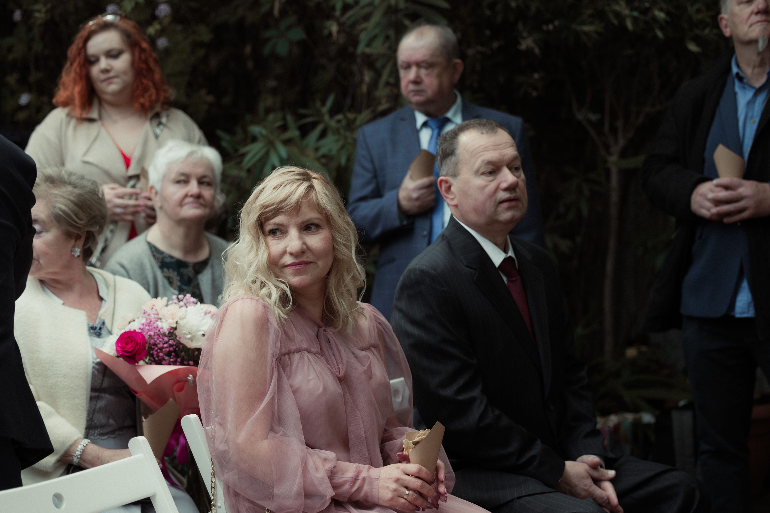 Wedding guests seated outdoors at a garden ceremony wearing formal attire.
