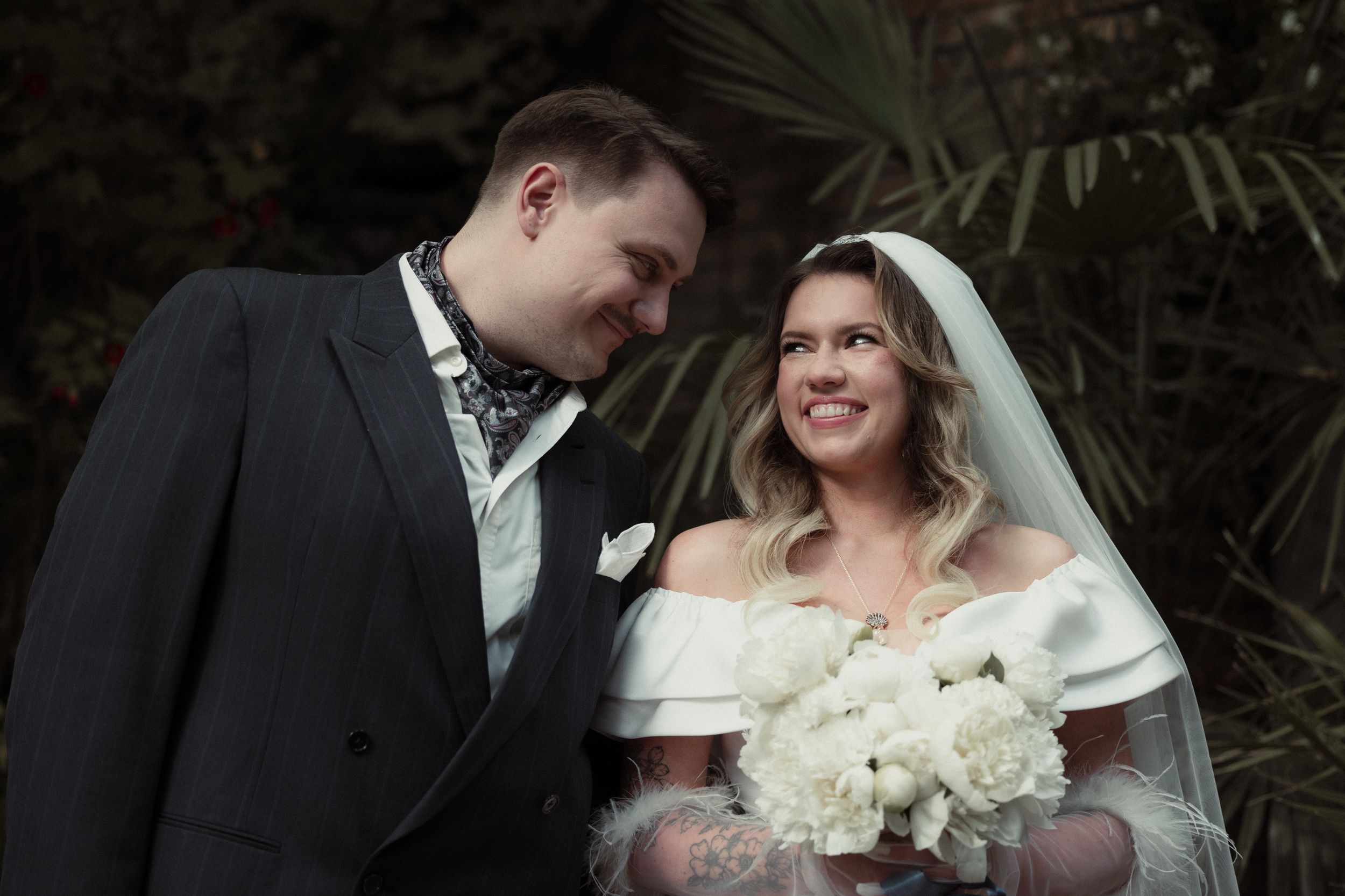 A happy couple shares a joyful moment at their wedding ceremony while holding a white floral bouquet.