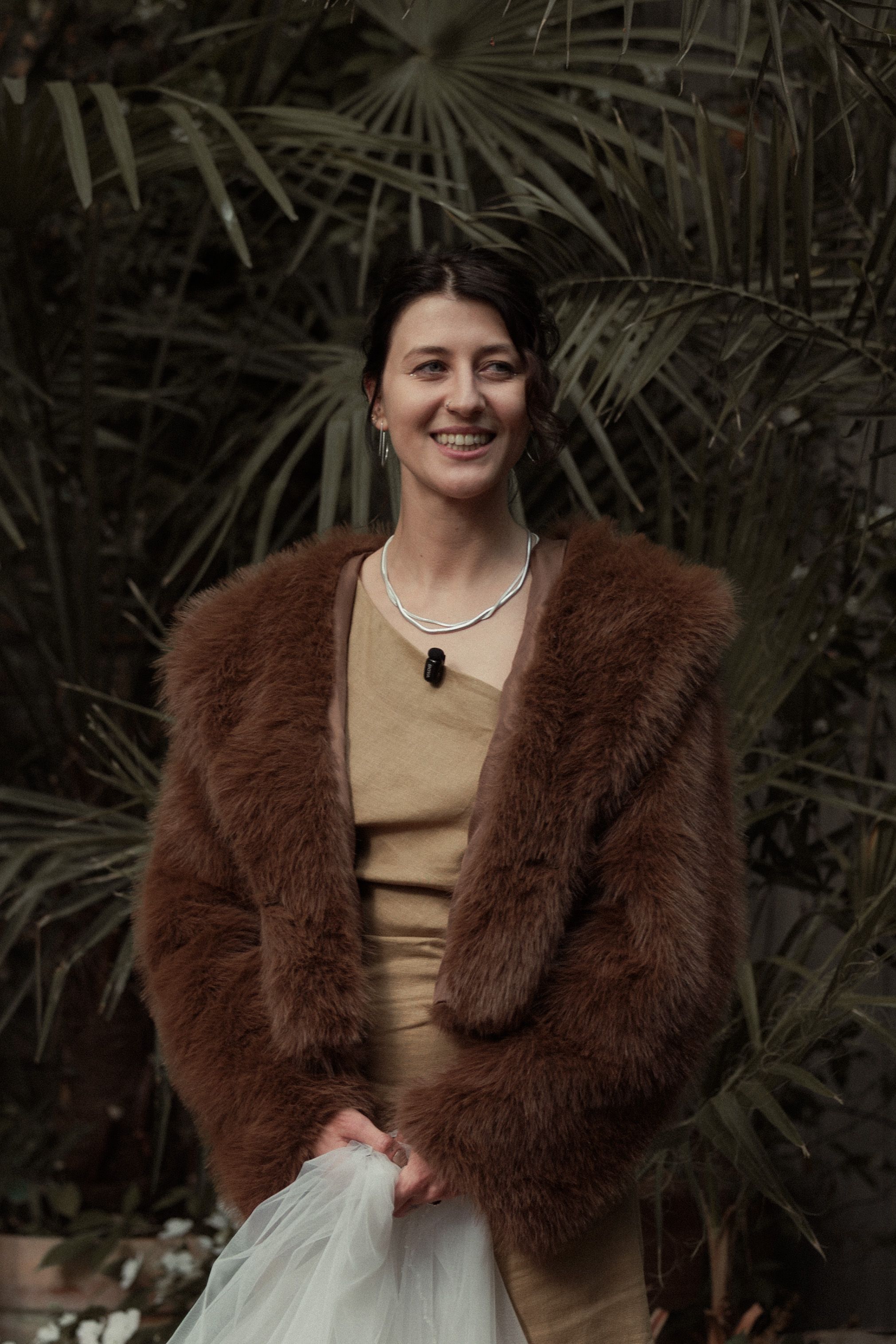 A brown faux fur coat paired with a beige outfit against a lush palm leaf background.