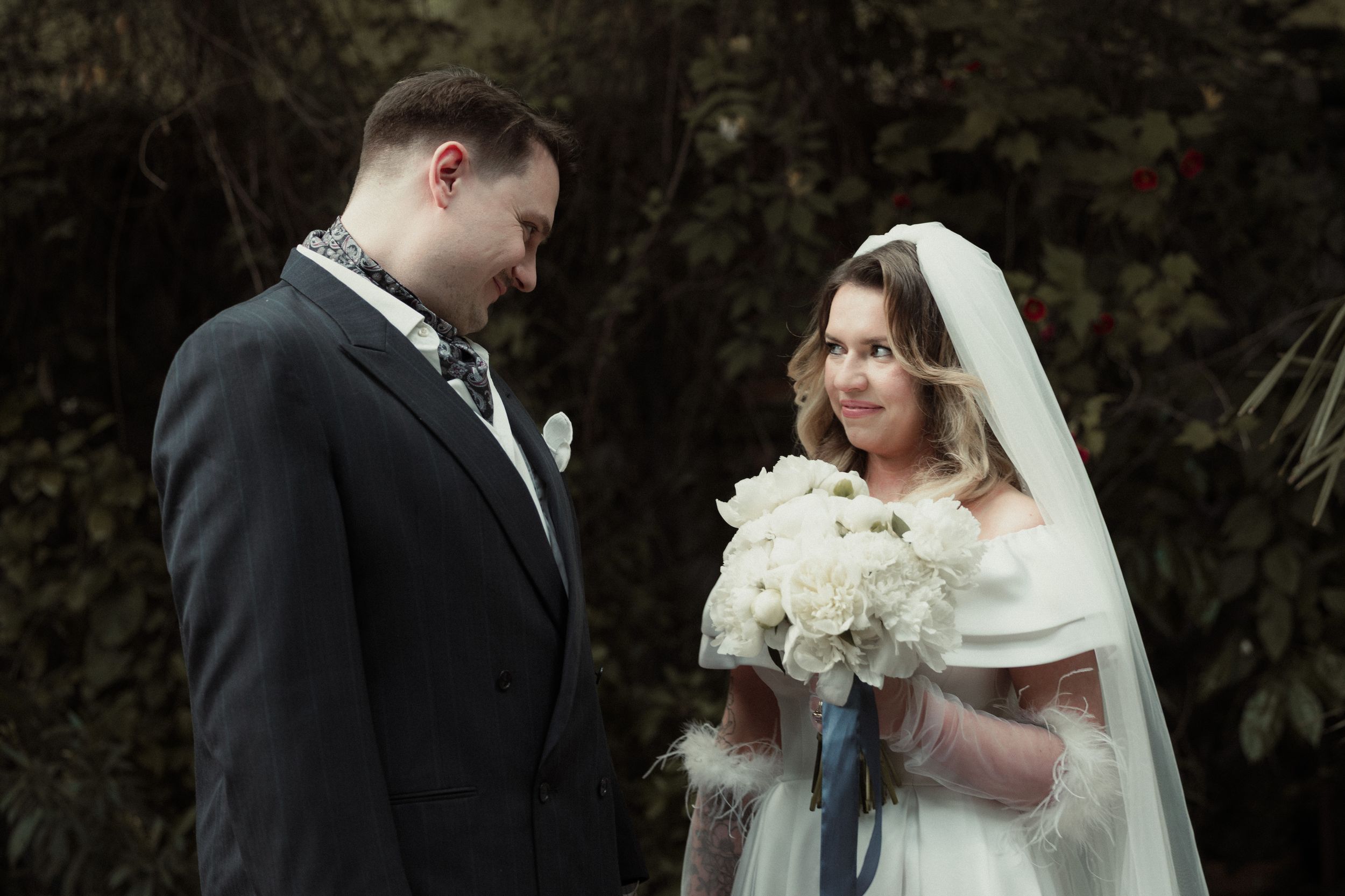 Bride and groom share a moment together during outdoor winter wedding ceremony while holding white bouquet.