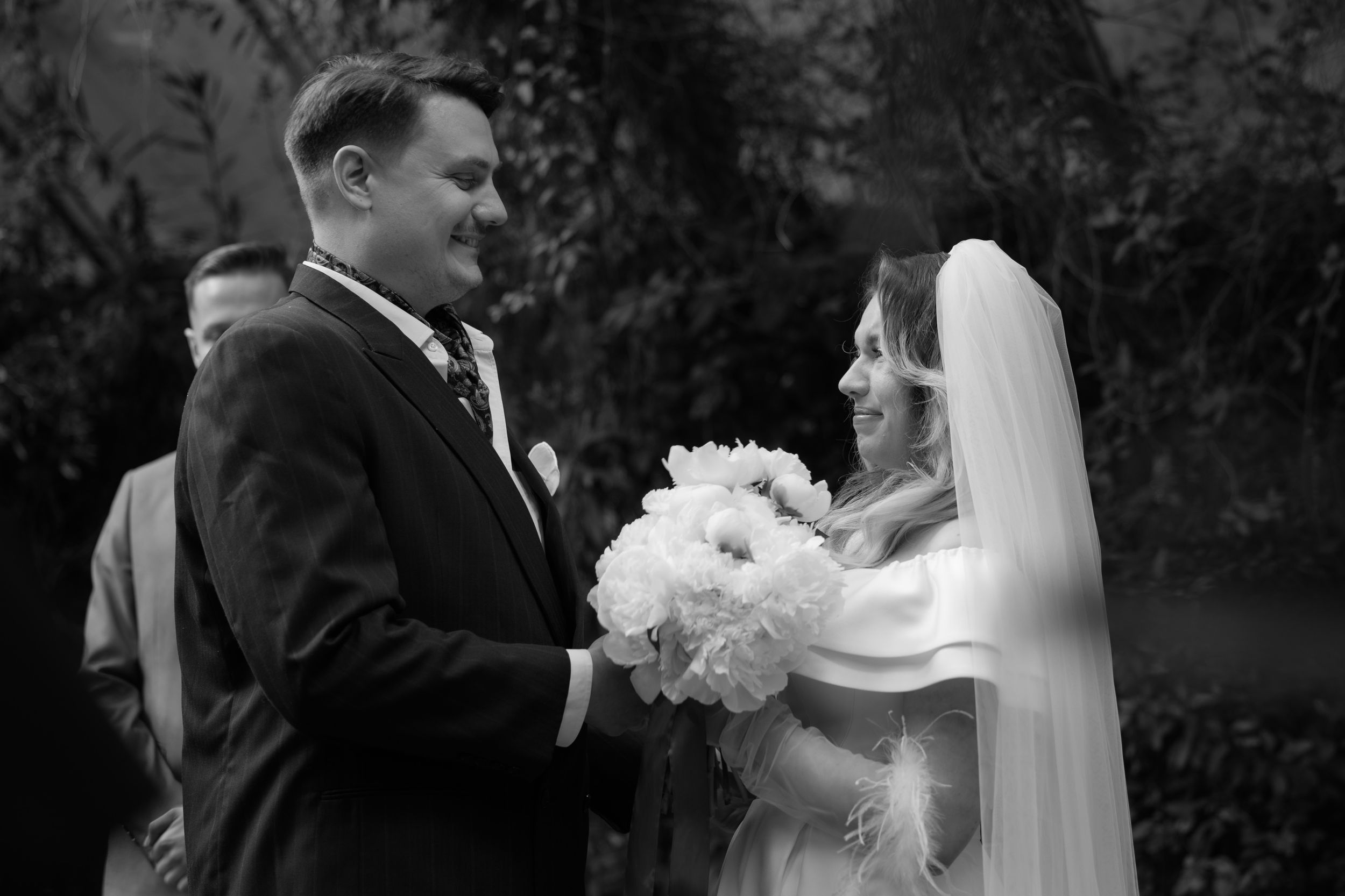 A black and white photo captures a tender moment between a bride and groom exchanging flowers during their wedding ceremony.