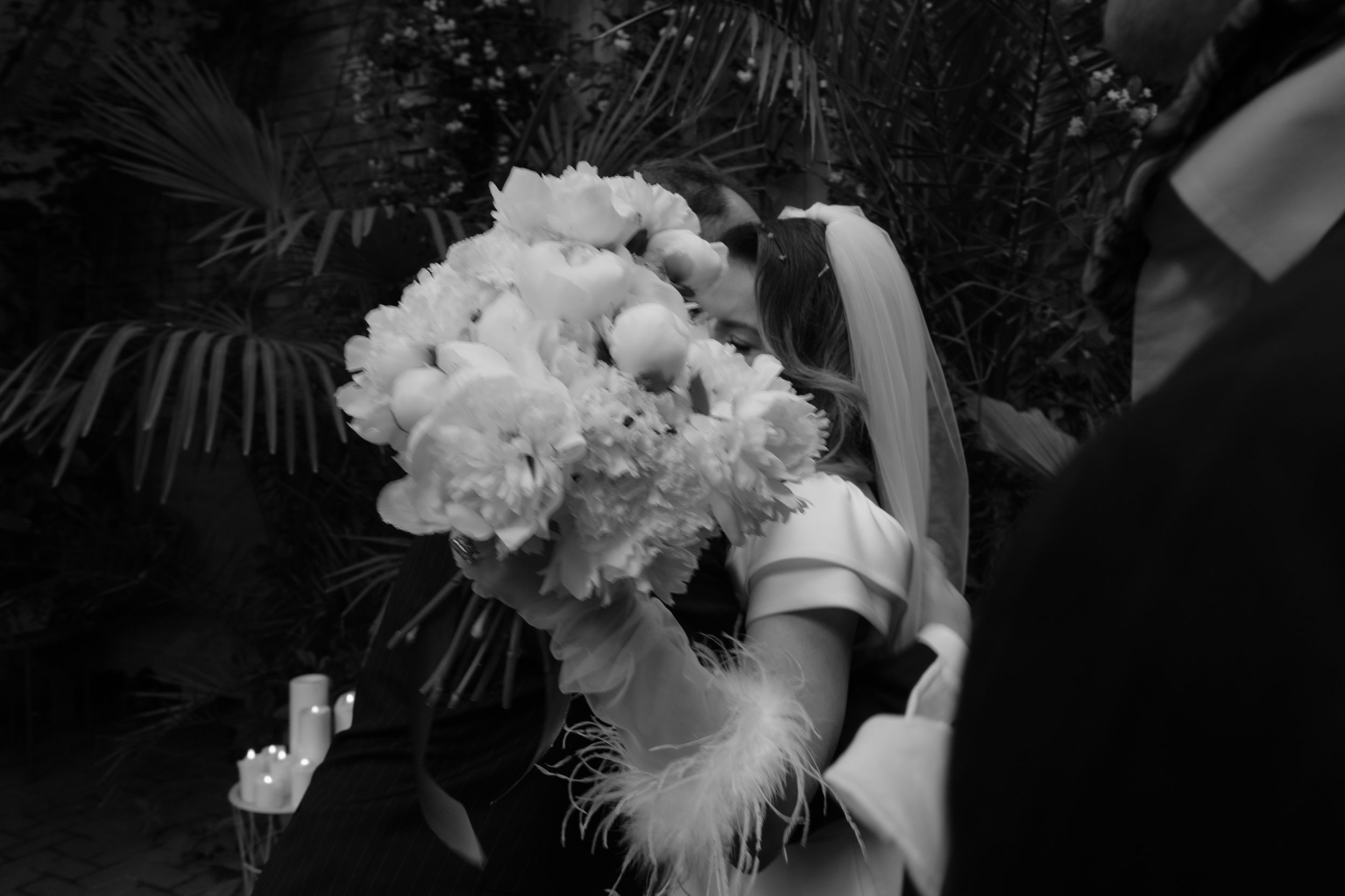 A black and white photograph showing a large bouquet of white carnations with feather accents being held.