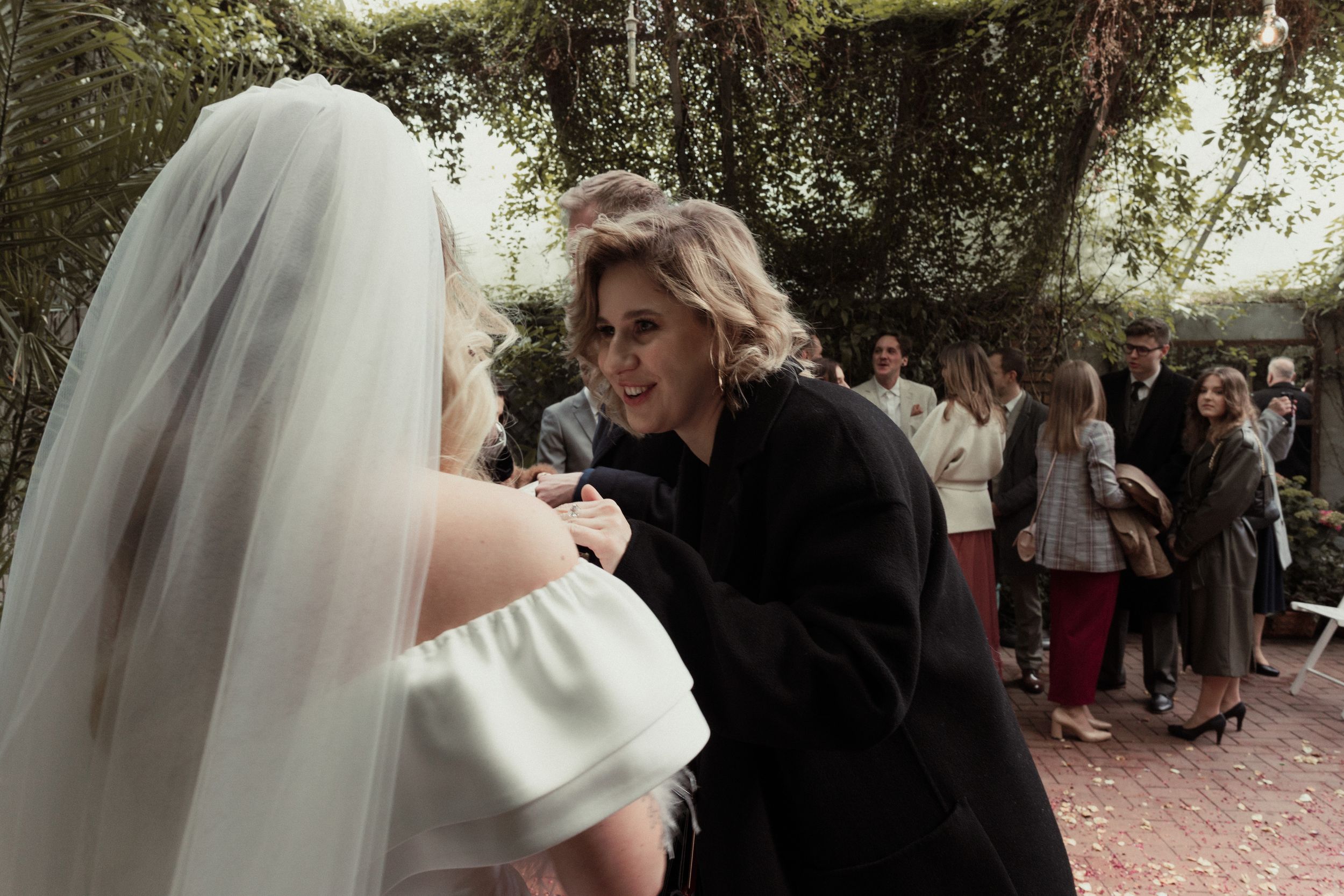Wedding celebration under trees with flowing white veils and guests gathered in an outdoor garden setting.