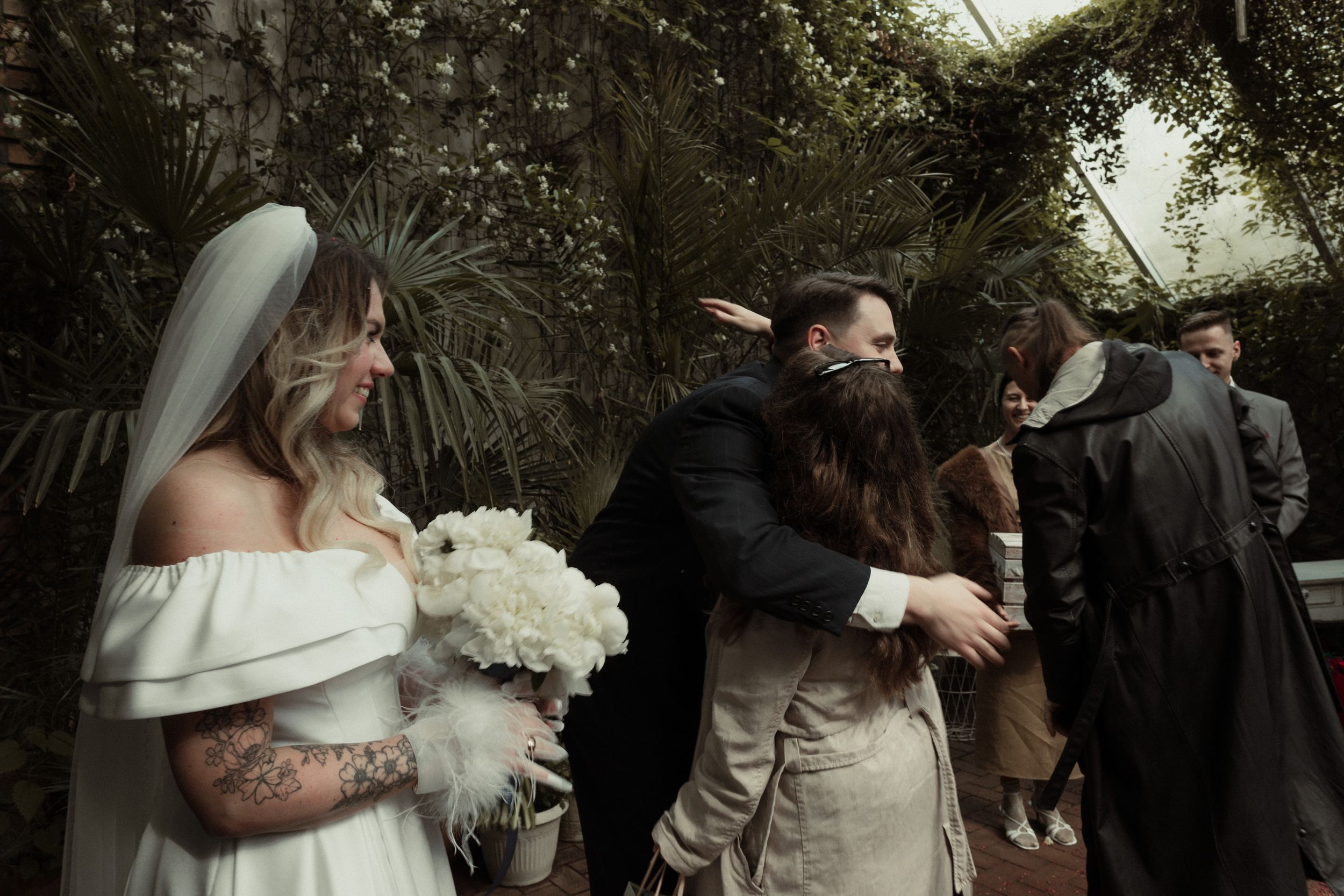 A couple shares an emotional embrace during a wedding ceremony in a lush outdoor garden setting.