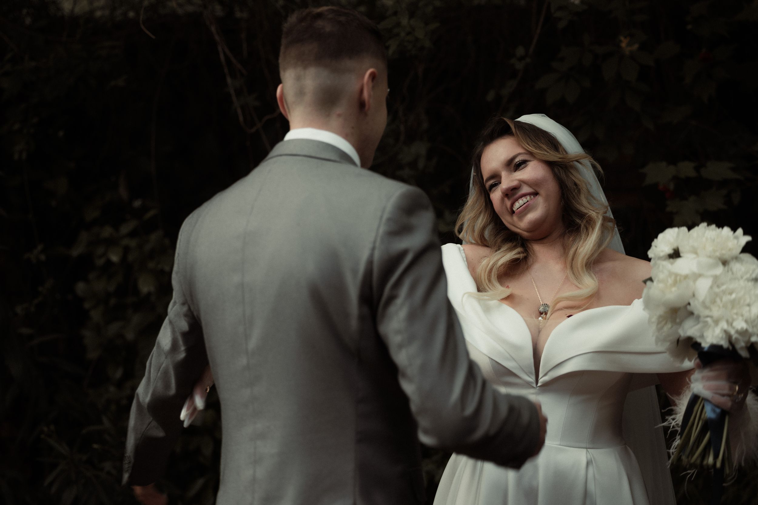 Romantic wedding couple dancing together in an outdoor garden setting with soft natural lighting and lush greenery background.