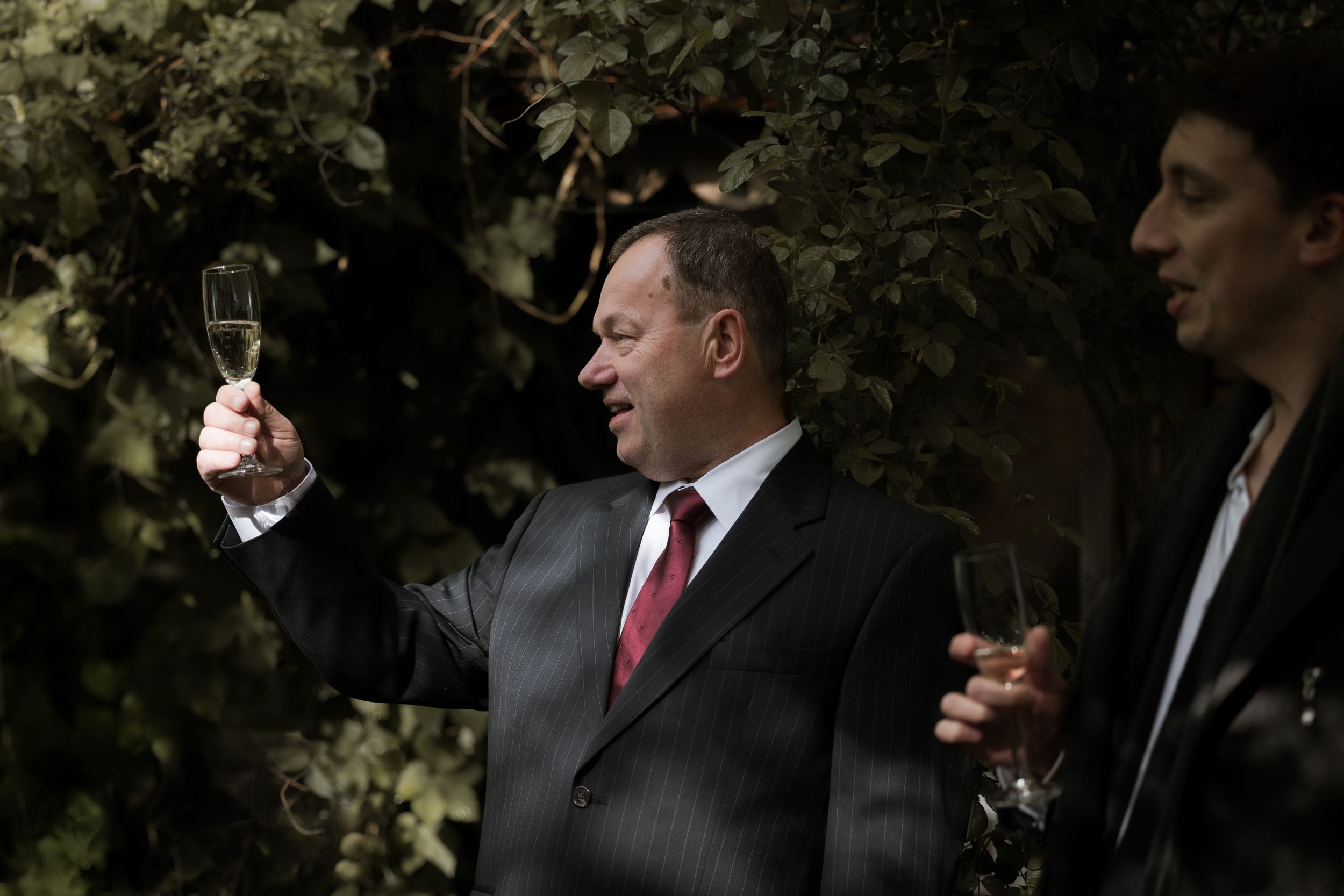 Two people in formal attire holding wine glasses during an outdoor gathering.