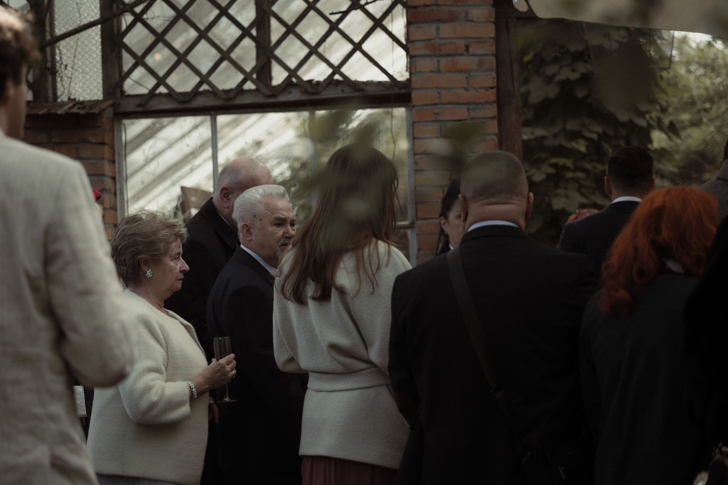 A group of people gathered at a social event beneath a brick and lattice structure in muted lighting.