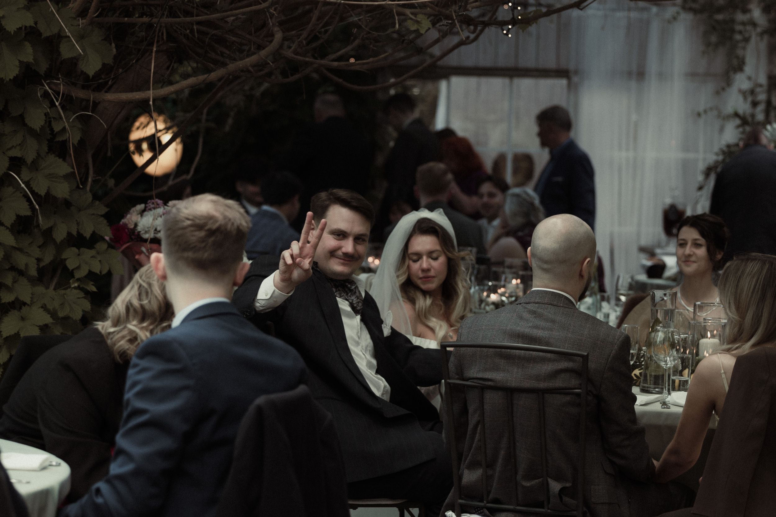 Stylish wedding guests enjoying conversation and drinks at an outdoor evening reception with romantic lighting.