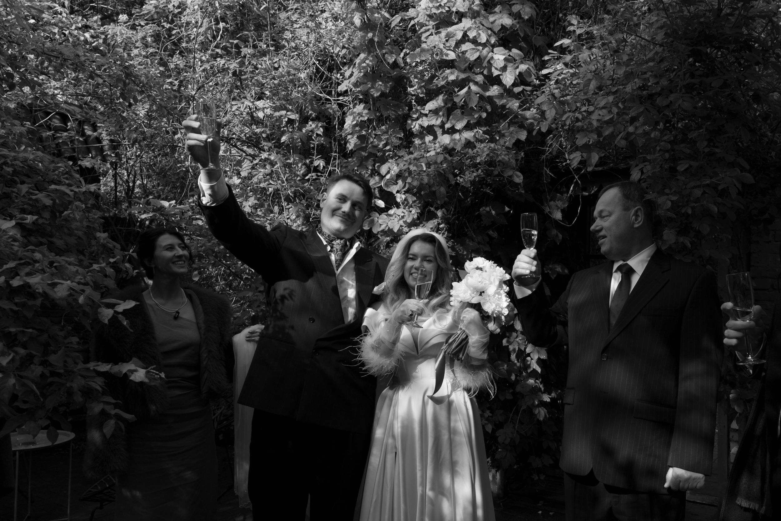 Vintage black and white photograph of a wedding celebration outdoors with group joyfully gesturing in a garden setting.