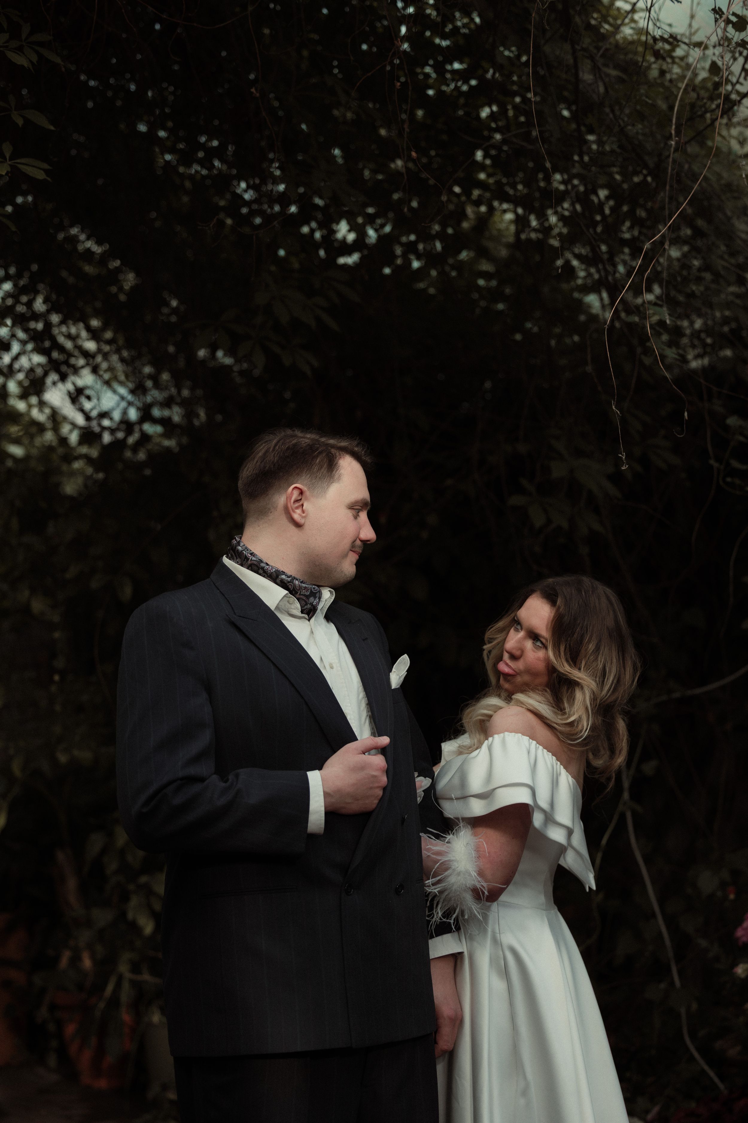 A romantic moment between newlyweds sharing laughter in an outdoor garden setting at dusk.