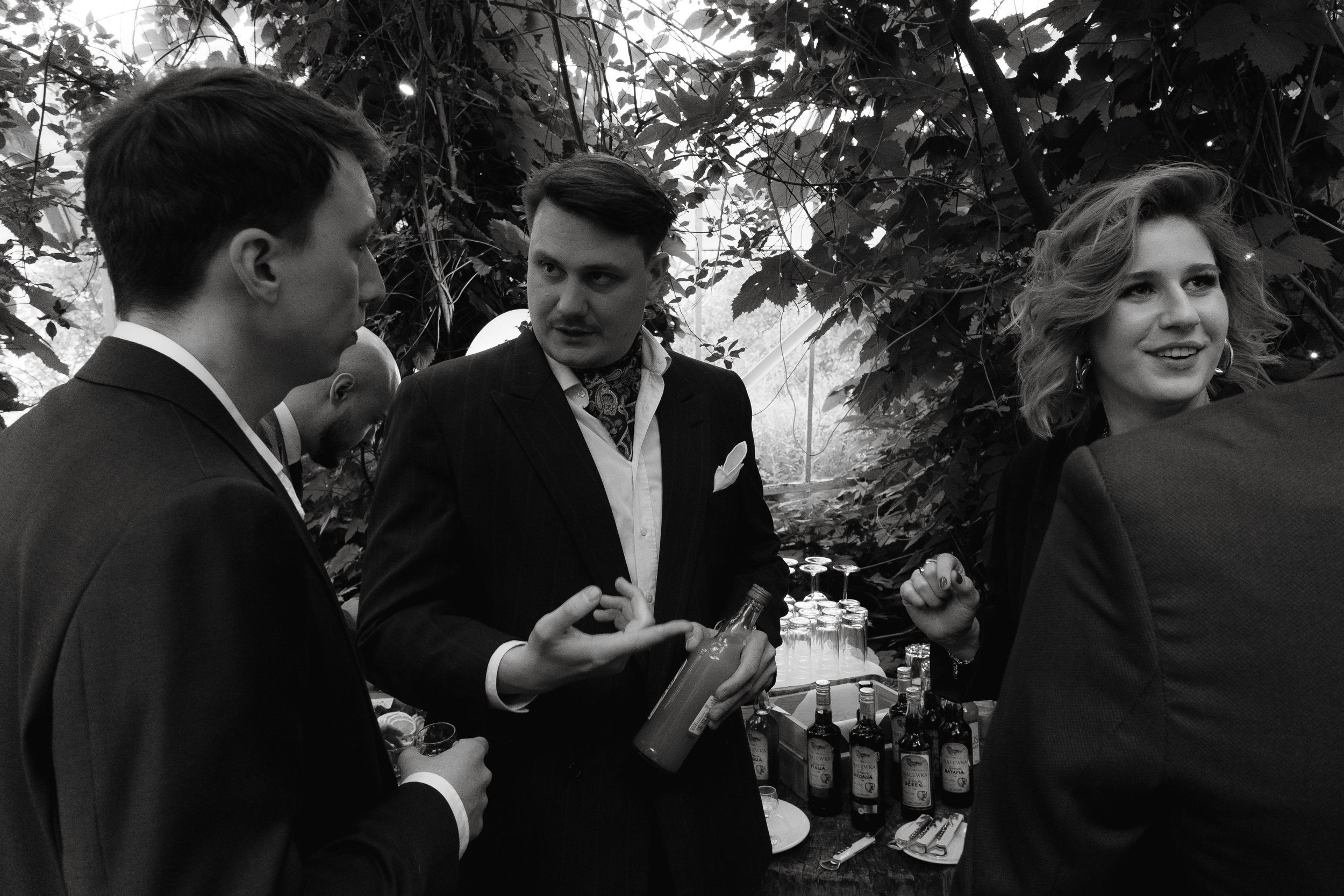 Black and white candid photo of three people engaged in conversation at an outdoor gathering.