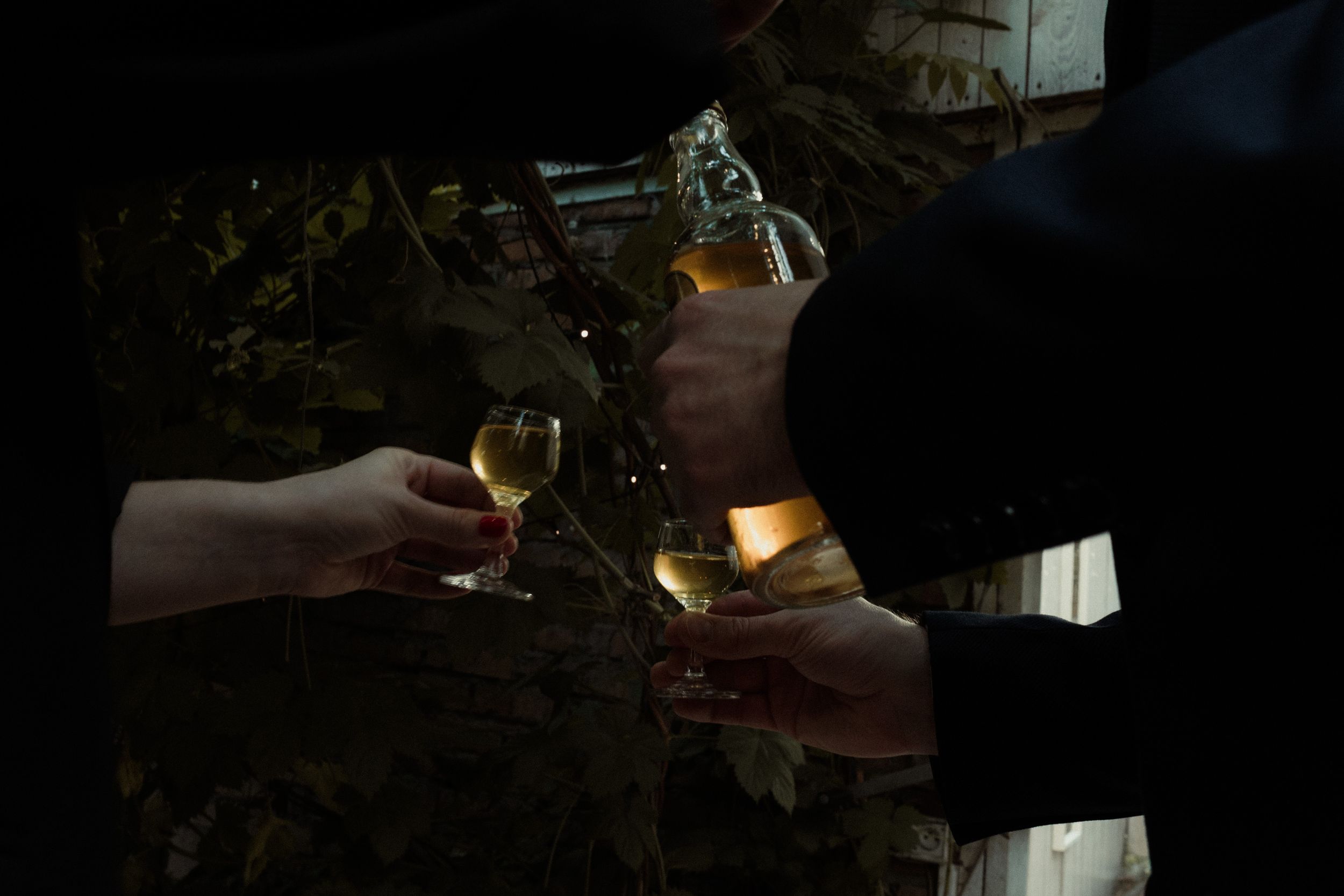Hands holding glasses of wine with glowing candles and warm ambient lighting in the background.