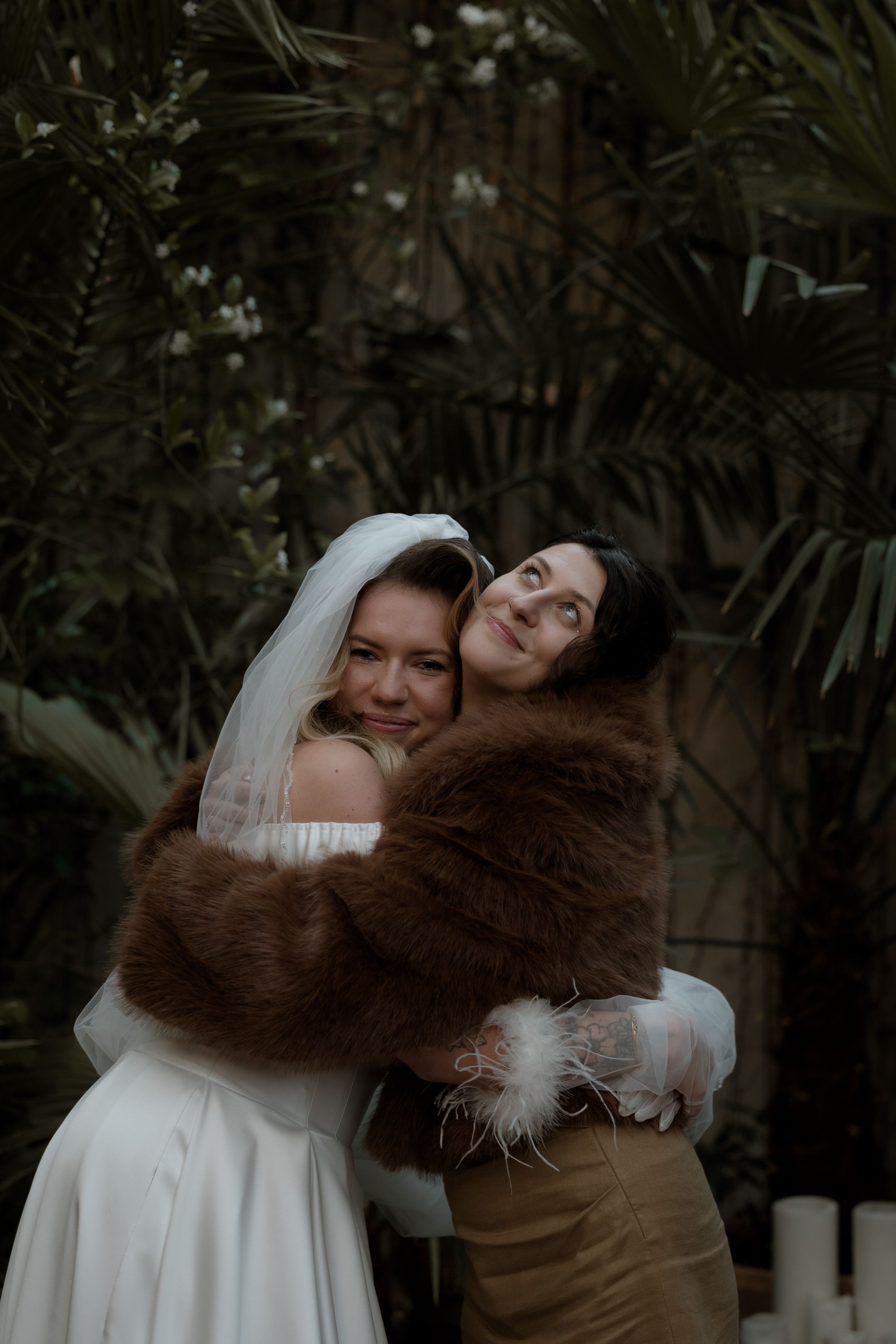 Two people share joyful embraces in a garden setting while wearing wedding attire.